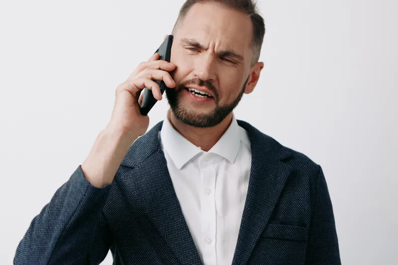 A professional businessman on a call, showing a tense and focused expression, isolated on a clean background. The scene conveys urgency, decision making, and communication under pressure.