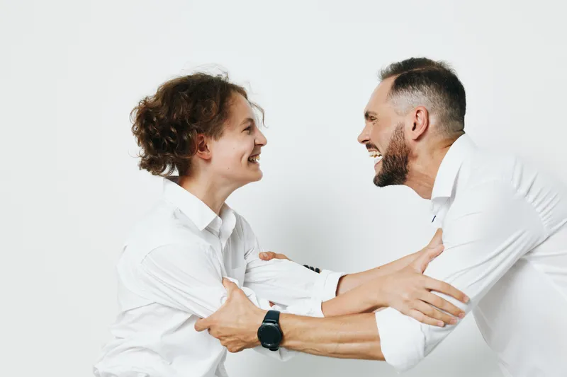 A professional man and colleague share a warm moment in a business setting, smiling and engaged, against an isolated white background, conveying teamwork and confidence.