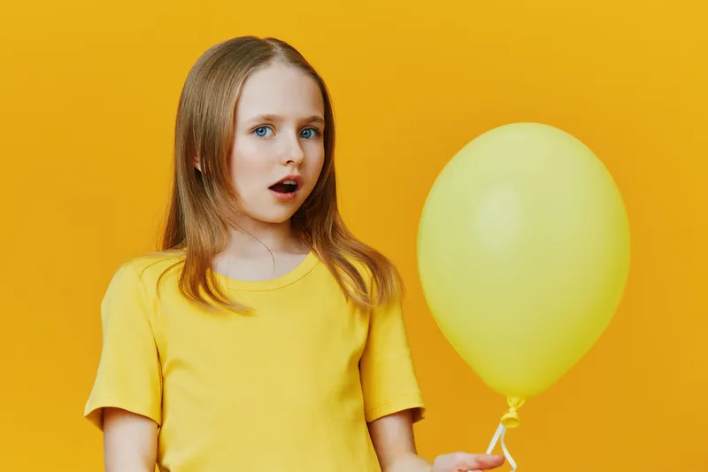Surprised girl with yellow balloon and yellow background, wearing a bright t shirt, expressing wonder in a colorful, cheerful setting