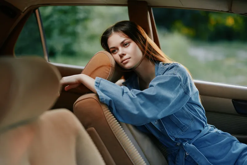 Young woman in denim attire expressing deep emotion while sitting in a vintage car, surrounded by nature, highlighting the concept of nostalgia and contemplation.
