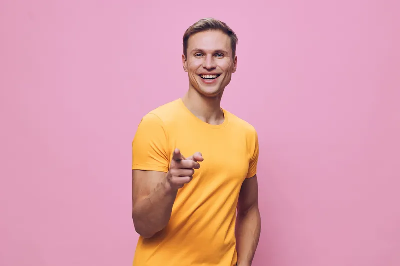 smiling man pointing finger in yellow t-shirt on pink background happy cheerful caucasian adult casual style digital detox concept
