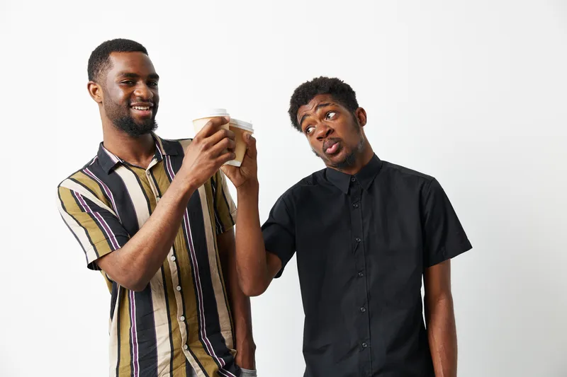 Two black men enjoying coffee together, sharing laughter and joy, showcasing friendship and camaraderie in a casual setting.