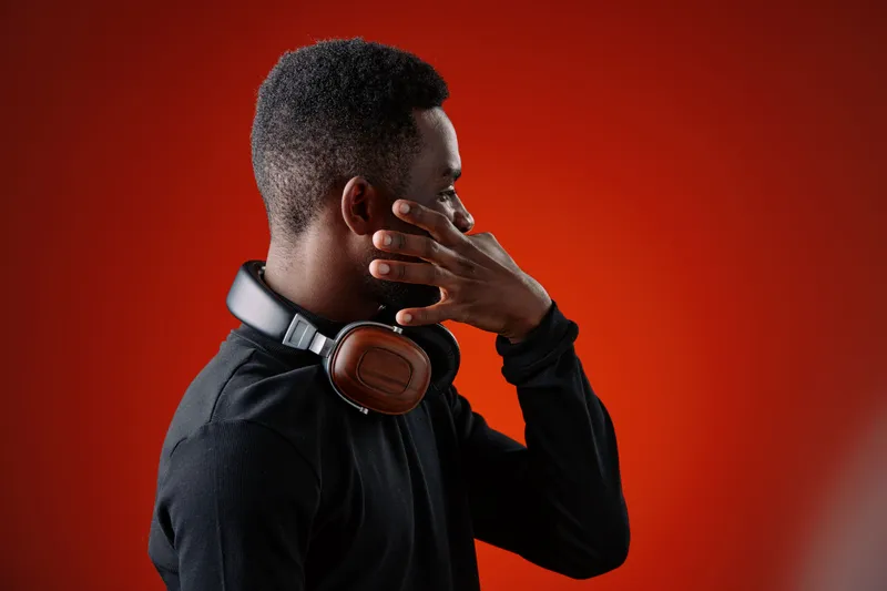 Young Black man enjoying music with headphones, wearing casual black attire, set against a vibrant red background, conveying relaxation and focus in a modern lifestyle