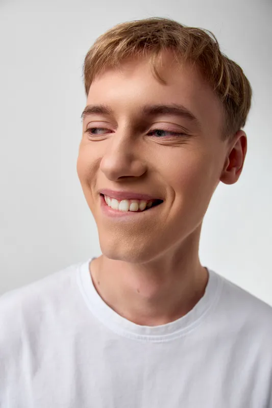 Smiling young man wearing a white shirt, casual style and warm expression, photographed in soft lighting for lifestyle, wellness and corporate branding projects