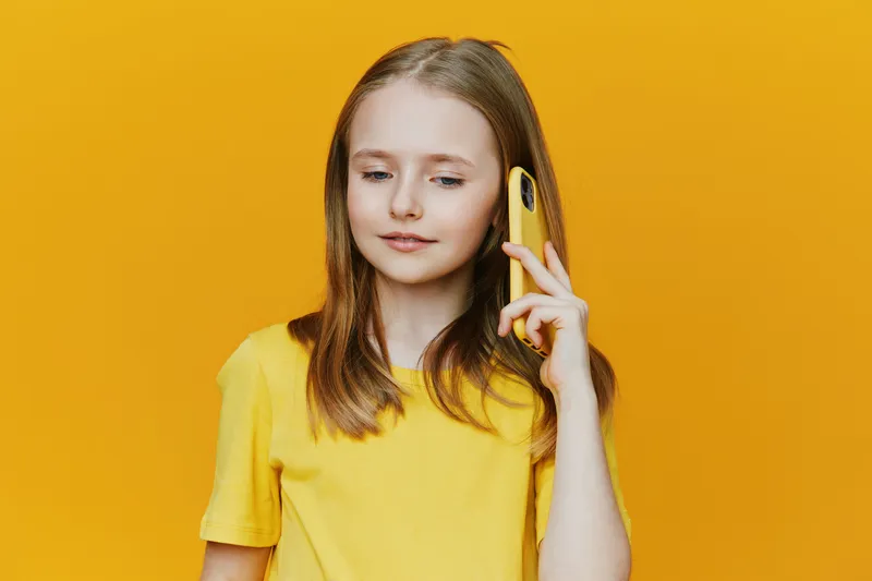 Young girl in yellow shirt talking on smartphone, bright yellow background, expressing joy and connection, ideal for communication concepts