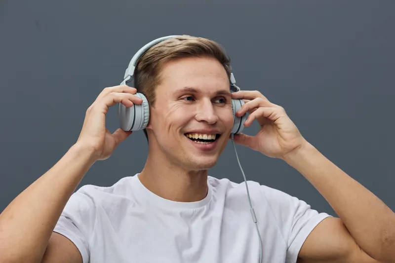smiling young caucasian man wearing headphones white t-shirt touching ear cup listening music isolated on gray background digital wellness mental health concept