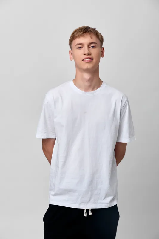 Casual youth in a white tshirt stands in a studio with relaxed posture, subtle smile, clean background, simple fashion and comfortable style for lifestyle and apparel photography.
