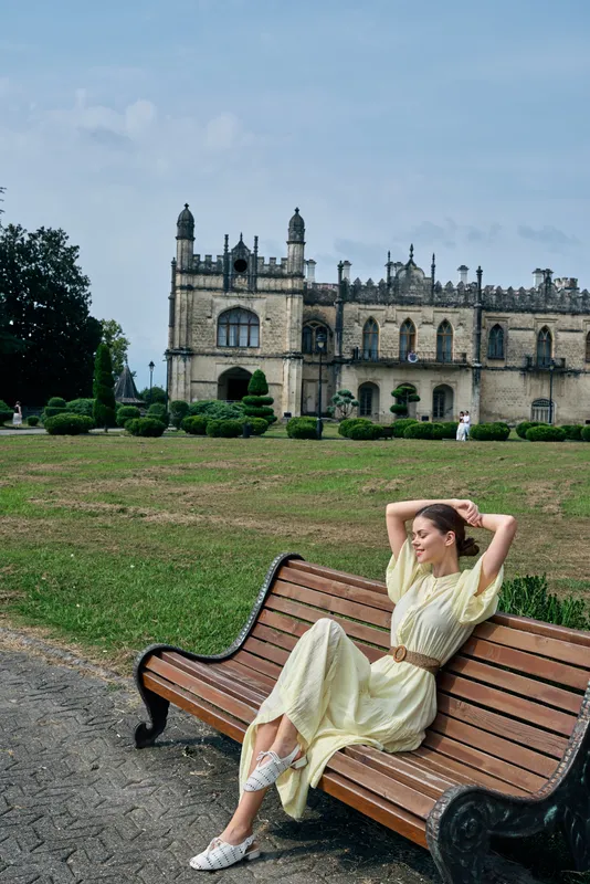 woman on bench in park with historic architecture, relaxing in flowing dress on lawn by grand building, portrait of authenticity and inclusivity, leisure moment and serene fashion