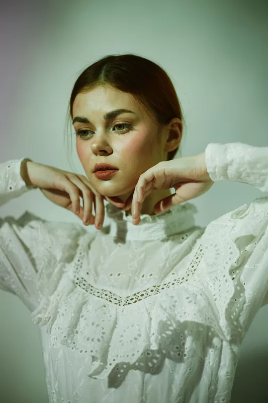 Young woman in a vintage white dress, posing gracefully, showcasing elegance and serenity against a soft green background, emphasizing beauty and style