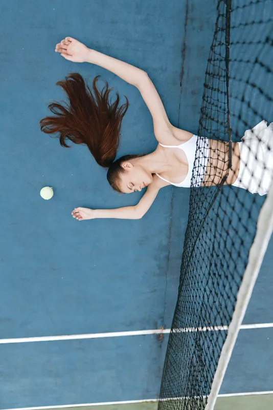 Athletic young woman in sportswear lying on a tennis court, showcasing emotions of relaxation and focus while surrounded by a vibrant blue background