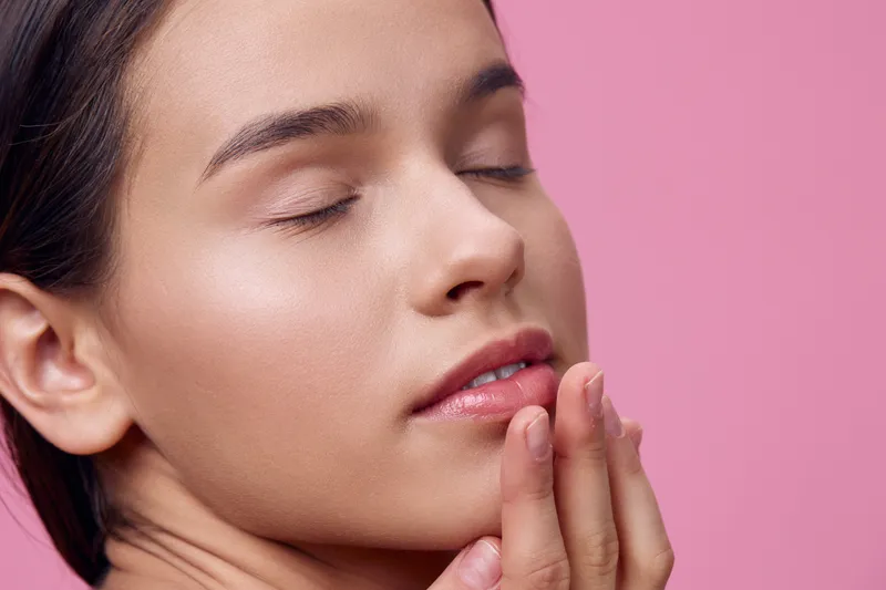 Close up of a serene young woman with closed eyes, showcasing natural beauty and soft skin against a pink background, conveying a sense of tranquility and self care