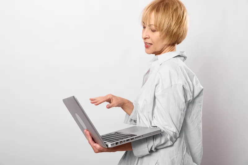 Woman using laptop, typing and smiling in bright studio light. Senior professional focuses on online work, remote communication, technology, and productivity today.