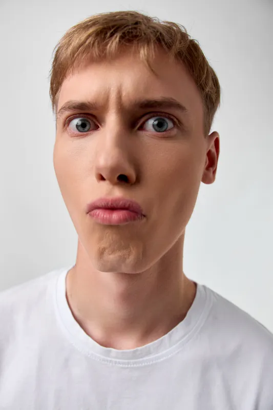 Puzzled expression on a closeup of a young man, wide eyes and pursed lips, capturing surprise, confusion, and curiosity in a simple studio setting for expressive stock imagery
