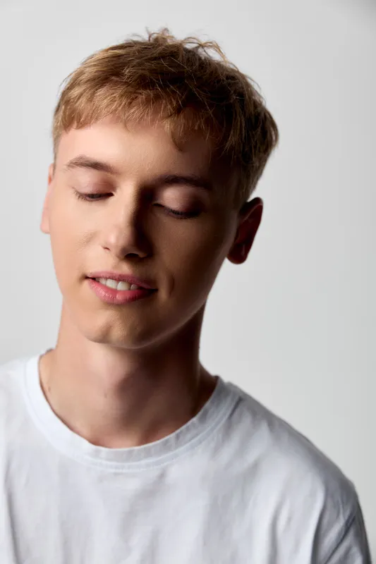 Young man with closed eyes and peaceful expression wearing a white tee, soft studio lighting enhances calm mood and serenity, minimal background highlights contemplation and inner peace in a clean,