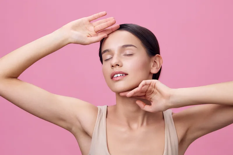 Young woman expressing joy in a soft pink background, wearing a light tank top, conveying positivity and confidence, perfect for wellness and beauty themes