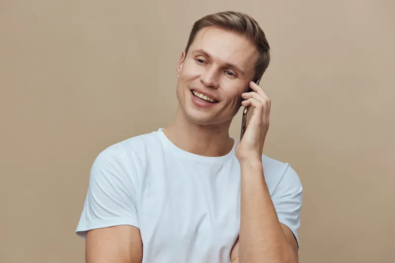smiling man talking phone wear white tshirt beige background casual look digital nomad concept communication technology lifestyle