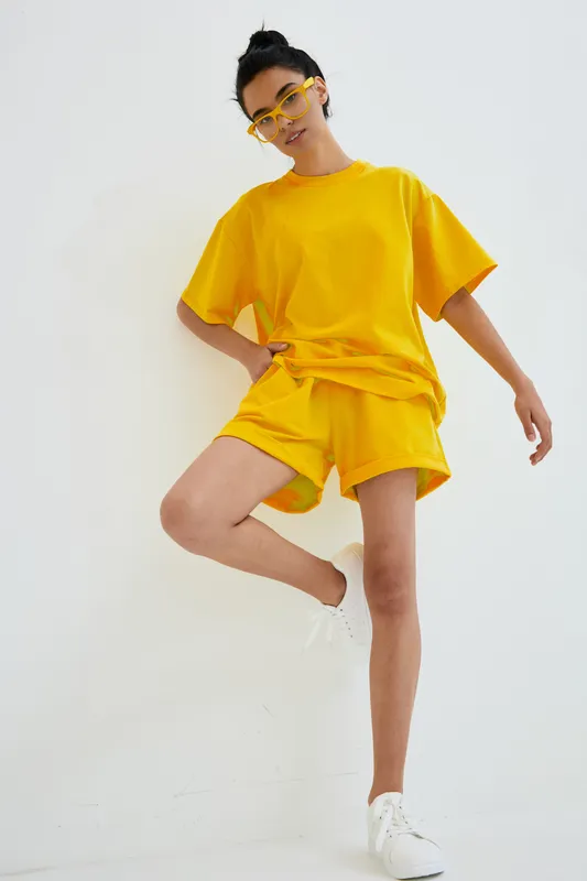 woman wearing bright yellow casual outfit posing against white background with stylish sunglasses and white sneakers, youthful and energetic mood