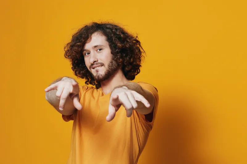 Young man with curly hair wearing a yellow shirt, expressing confidence and happiness against a vibrant yellow background, perfect for cheerful lifestyle themes