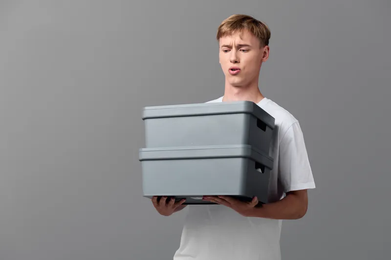 Man in a white shirt holds a stack of grey boxes for delivery, packaging and shipping, showcasing loading, warehousing and logistics in action, a clean studio setup highlighting inventory management