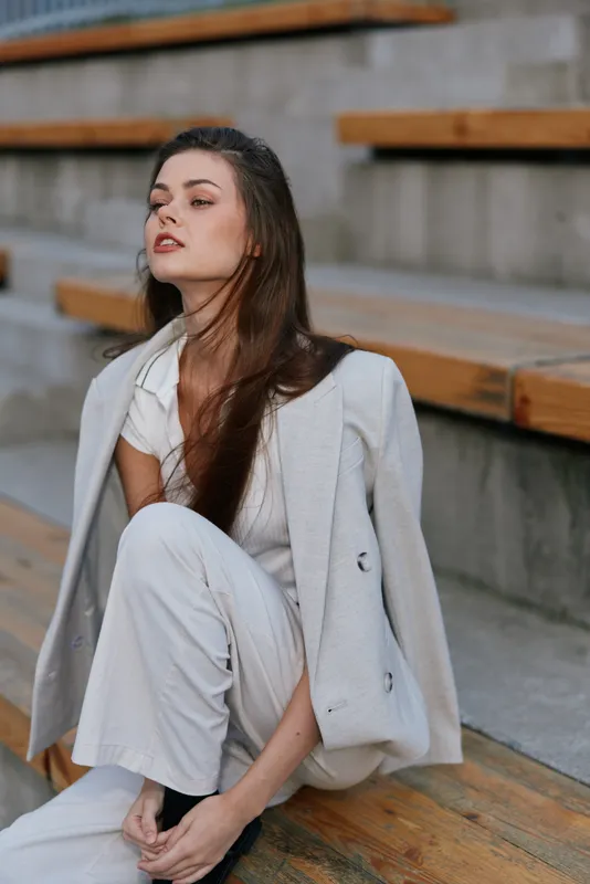 Businesswoman in a modern outfit conveying confidence and poise, seated on wooden steps with a stylish demeanor.