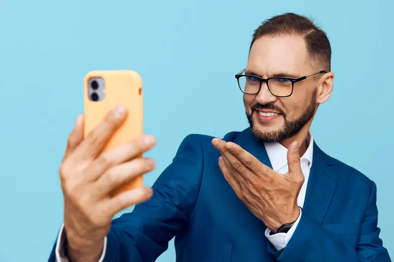 Professional businessman portrait on a vibrant blue background, isolated color. He smiles confidently while taking a selfie, conveying enthusiasm, focus, and approachable leadership in a modern work