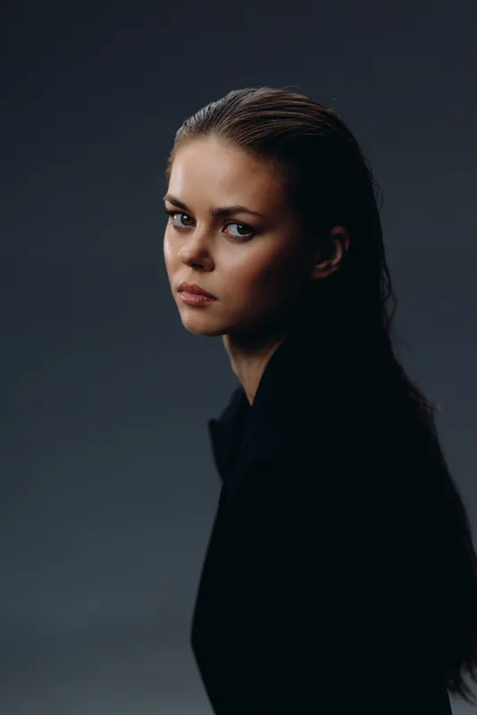 Portrait of a serious woman with wet hair and dark clothing in a moody studio setting.