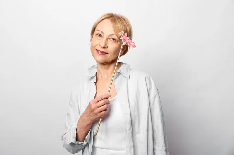 Woman smiling pink flower studio portrait hair white elegant selfcare, beauty wellness spring freshness, white blouse, soft studio lighting, soft backdrop