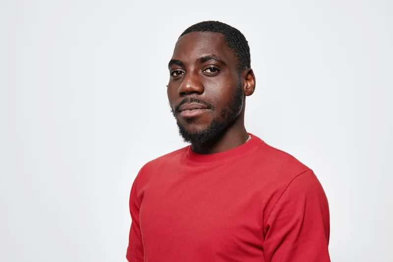Portrait of confident black man with dark skin wearing red sweater looking at camera isolated on white background. African ethnicity, casual style and facial hair visible.