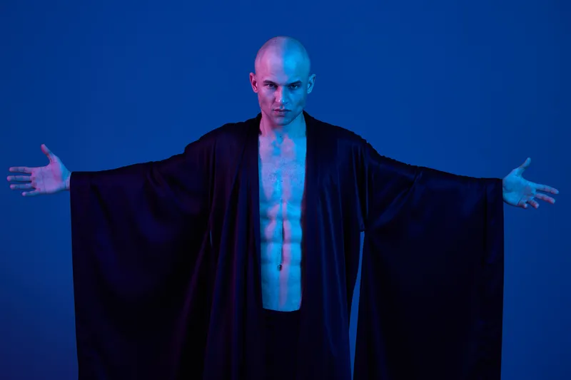 Confident man in dark robe, showcasing strength with blue lighting. Perfect for artistic and dramatic compositions, emphasizing bold expressions and contrast.