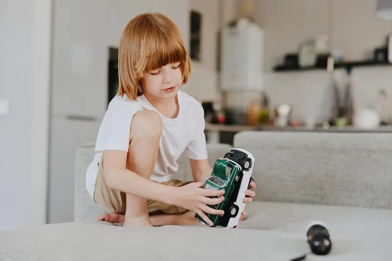 A young boy is playing with a toy car in a bright living room, showcasing creativity and imagination in a cozy environment filled with warmth and light.