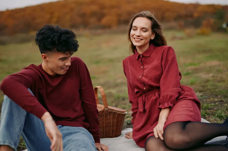 A genuine candid portrait of a young couple enjoying an autumn picnic outdoors, relaxed and smiling on a blanket with a wicker basket, conveying authenticity and natural credibility in the scene.