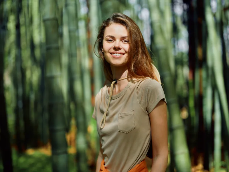woman smile bamboo forest portrait outdoors nature sunlight on her face, young female standing among green stalks, relaxed casual clothing and happy candid expression in warm summer woods