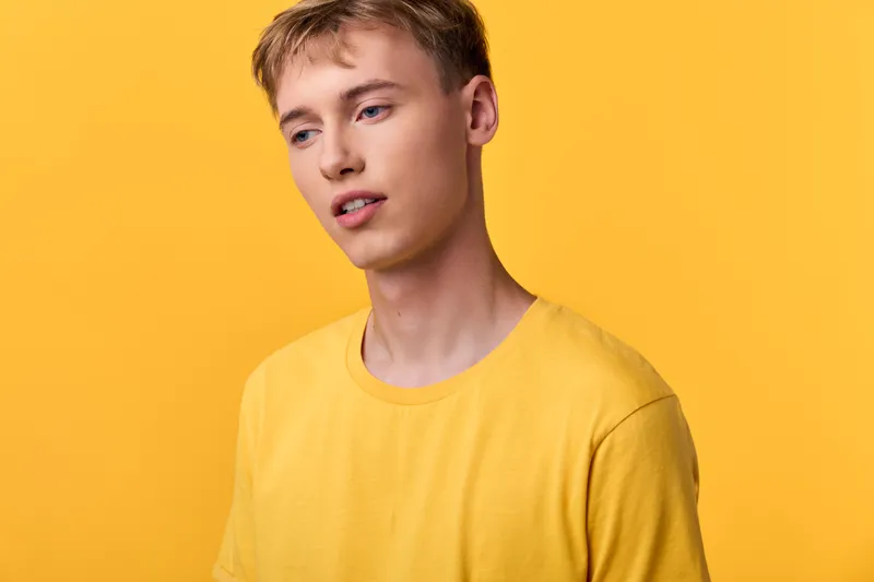Young man in a bright yellow shirt against a solid yellow backdrop, studio shot with a minimalist style, warm lighting and casual mood for fashion imagery