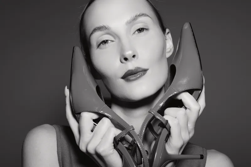 Portrait of a fair skinned Caucasian woman holding high heels near her face against a dark studio background, fashion and beauty concept.