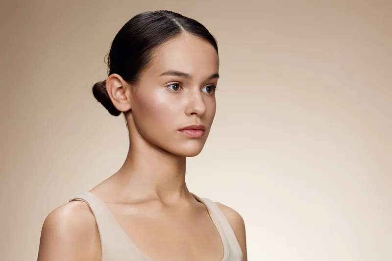 Elegant portrait of a young woman with a neutral expression, featuring soft lighting and a beige background, ideal for beauty and skincare concepts