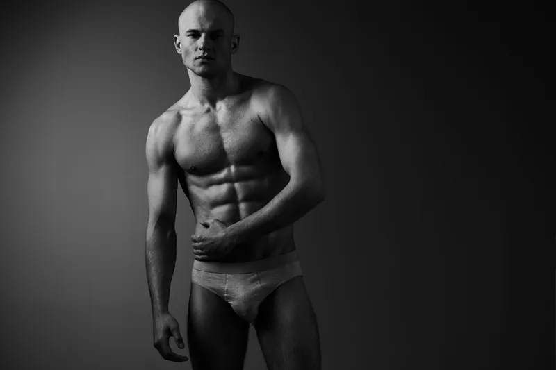 Athletic man posing in black and white photography, showcasing toned muscles and confident expression, focusing on strength and grace.