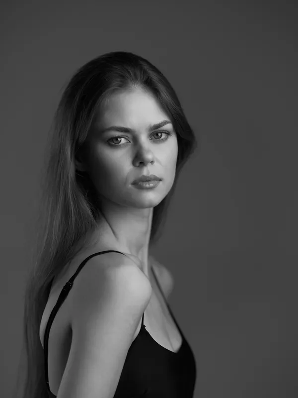 Black and white portrait of a serious young woman with long hair wearing a black top against a dark background