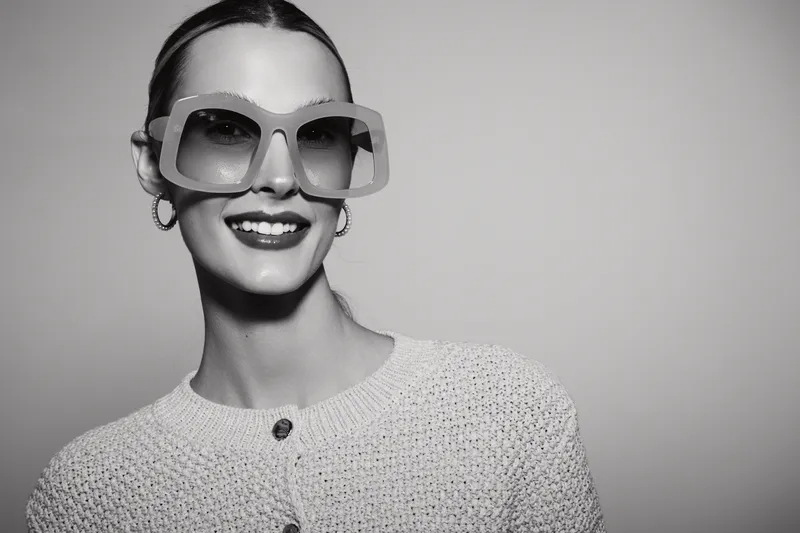 Smiling Caucasian woman with light skin wearing oversized sunglasses and knitted cardigan in a studio portrait, fashion and style concept.