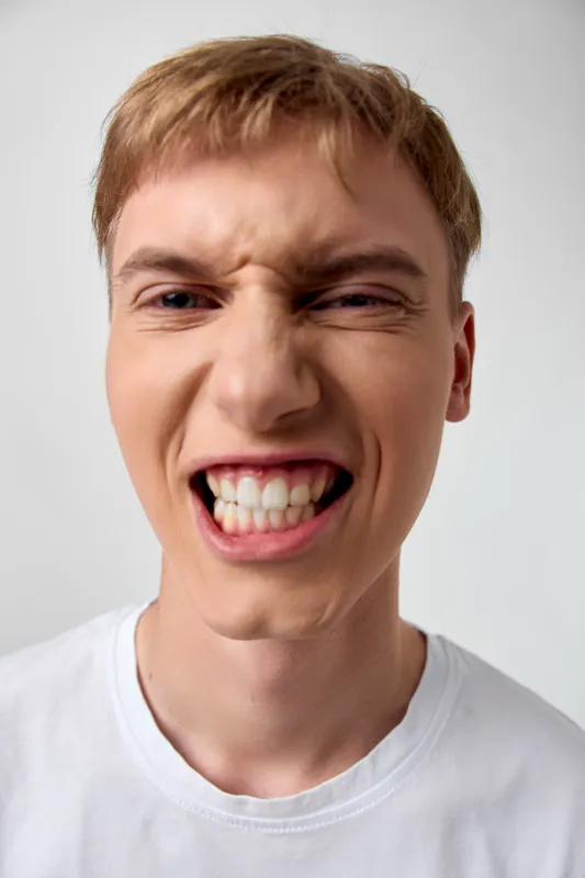 Close up of a tense young man with a clenched jaw and bared teeth, showing anger and frustration in a high energy facial expression for dramatic, intense moments