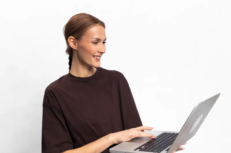 Smiling woman in casual dark t shirt using laptop computer isolated on white background. Concept of remote work, technology, and communication in modern lifestyle.
