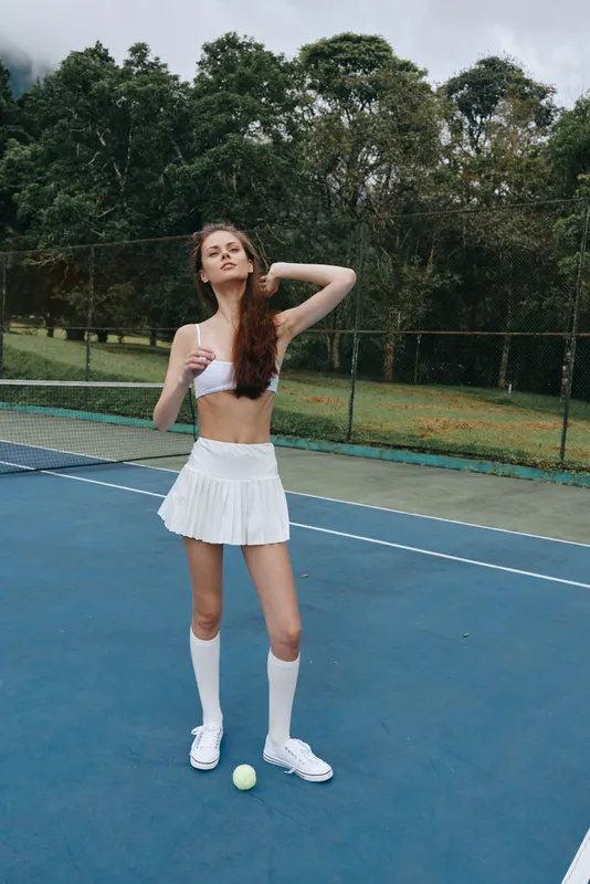 Young athletic model in a sporty outfit poses confidently on a tennis court, showcasing determination and style, with green trees in the background
