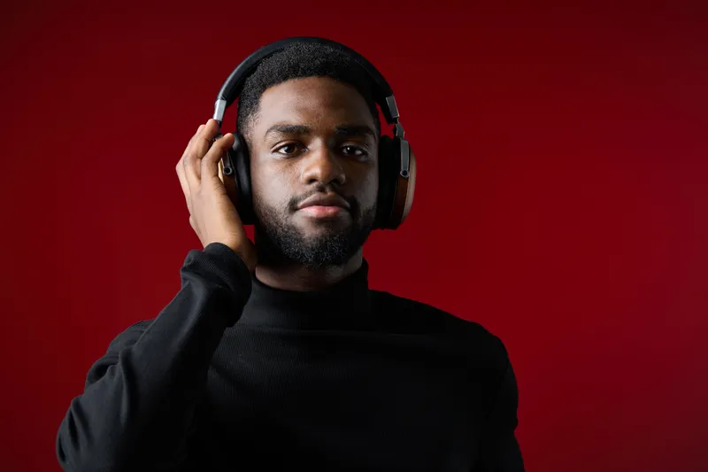 Young Black man wearing headphones, enjoying music against a rich red backdrop, exuding a vibe of relaxation and modern style, perfect for lifestyle and music themes