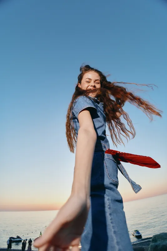lifestyle woman in modern boho-western denim street style smiling with red bandana near seaside under clear blue sky film color tone