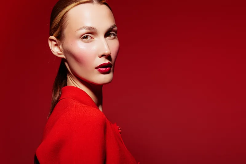 Portrait of a woman with red lipstick and red clothing against a red background. The image highlights fashion, beauty, makeup, and confident expression in a studio setting.