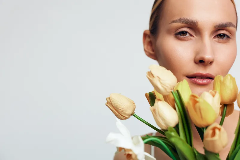 Closeup portrait of a woman holding yellow tulips bouquet, soft natural light, neutral background, calm expression, fresh flowers, spring mood, minimalistic style