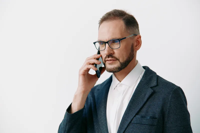 A focused business professional man on a call, standing against an isolated colored backdrop. He exudes concentration and confidence, portraying a corporate moment of decision, communication, and