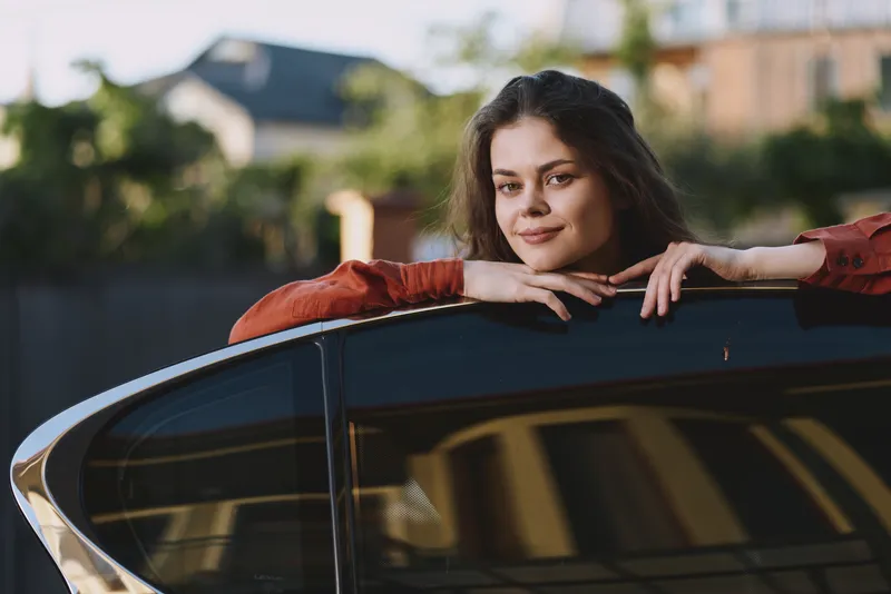 Woman leans on a car window in a casual outdoor setting, presenting a relaxed lifestyle, natural smile, and confident pose suitable for portrait and everyday moments