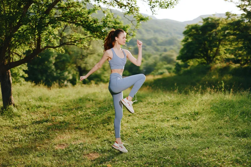 Athletic young woman exercising outdoors in a green landscape, wearing light blue activewear, showcasing joy and energy in a summer setting