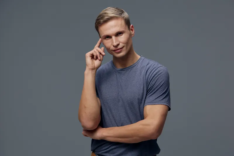 thoughtful man with blue t-shirt finger on temple look camera standing on grey background mental health and gadgets concept