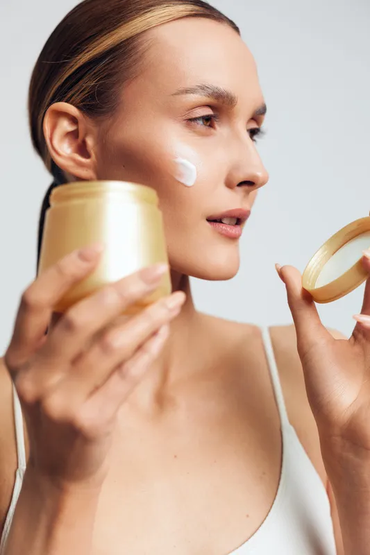 Young woman applying moisturizing cream on her cheek, skincare routine, natural beauty, soft lighting, smooth skin, close-up portrait, minimal makeup, healthy lifestyle.